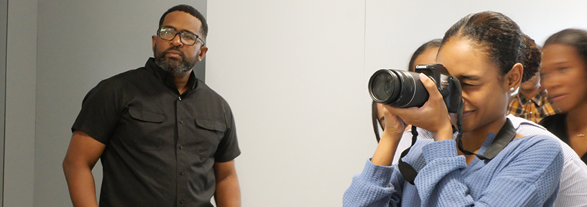 Docente junto a estudiante que utiliza una cámara. 