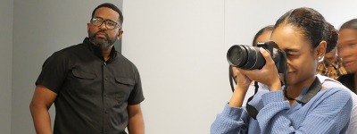 Docente junto a estudiante que utiliza una cámara. 